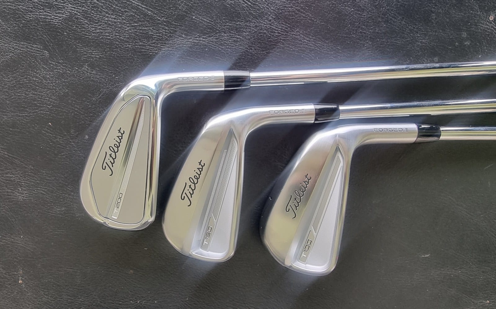 Three Titleist iron heads laid side by side, badged T200, T150 and T100 across the back cavity.