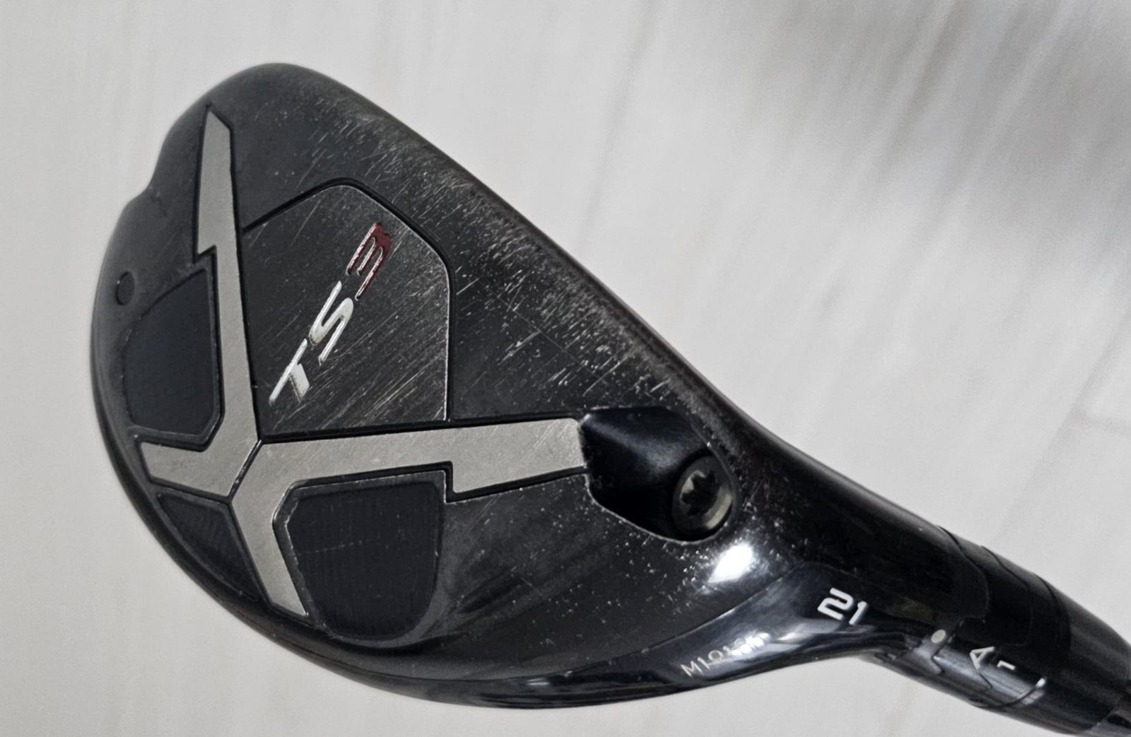 A Titleist TS3 hybrid head photographed from the sole, with the model name TS3 on the badge and the number 21 stamped near the hosel.