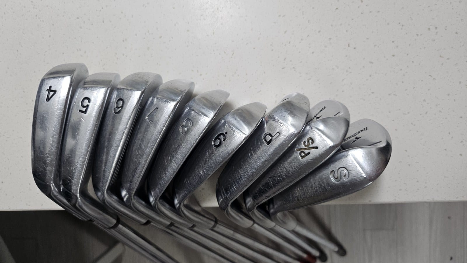 Nine Tourstage V300 III irons lined up, sole numbers 4 through S facing the camera and the Tourstage name visible on the wedge heads.