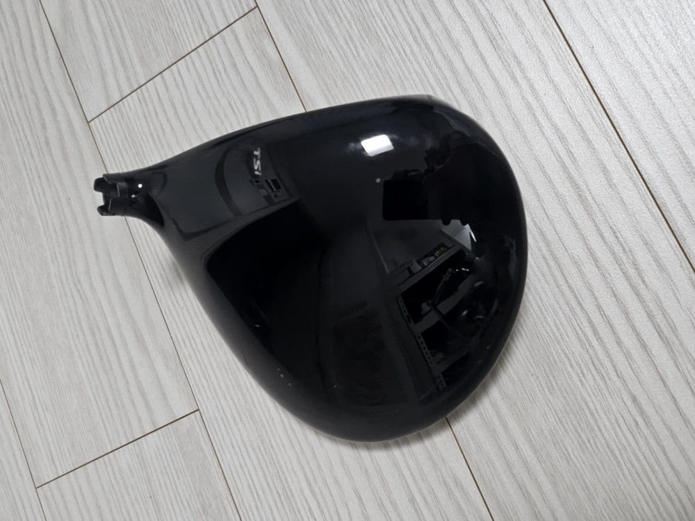 The sole of a black driver head photographed on a wooden floor.