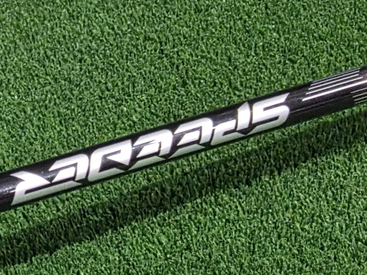 A close-up of a black Speeder driver shaft lying across practice turf, the brand graphic running along the shaft.