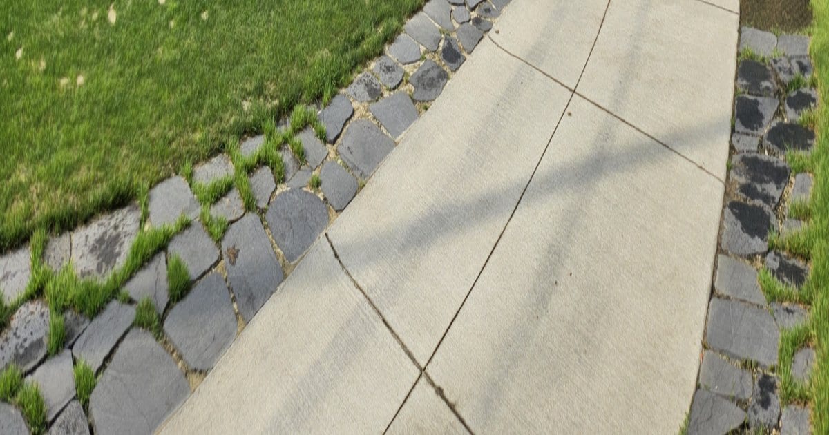 A paved cart path photographed from above, edged on both sides with dark stone setts, with mown grass running up to the stone on the left.