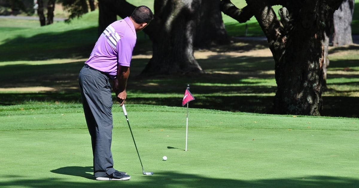 A golfer standing over a short putt on a green, the ball in front of the putter head and the flagstick a few paces away.