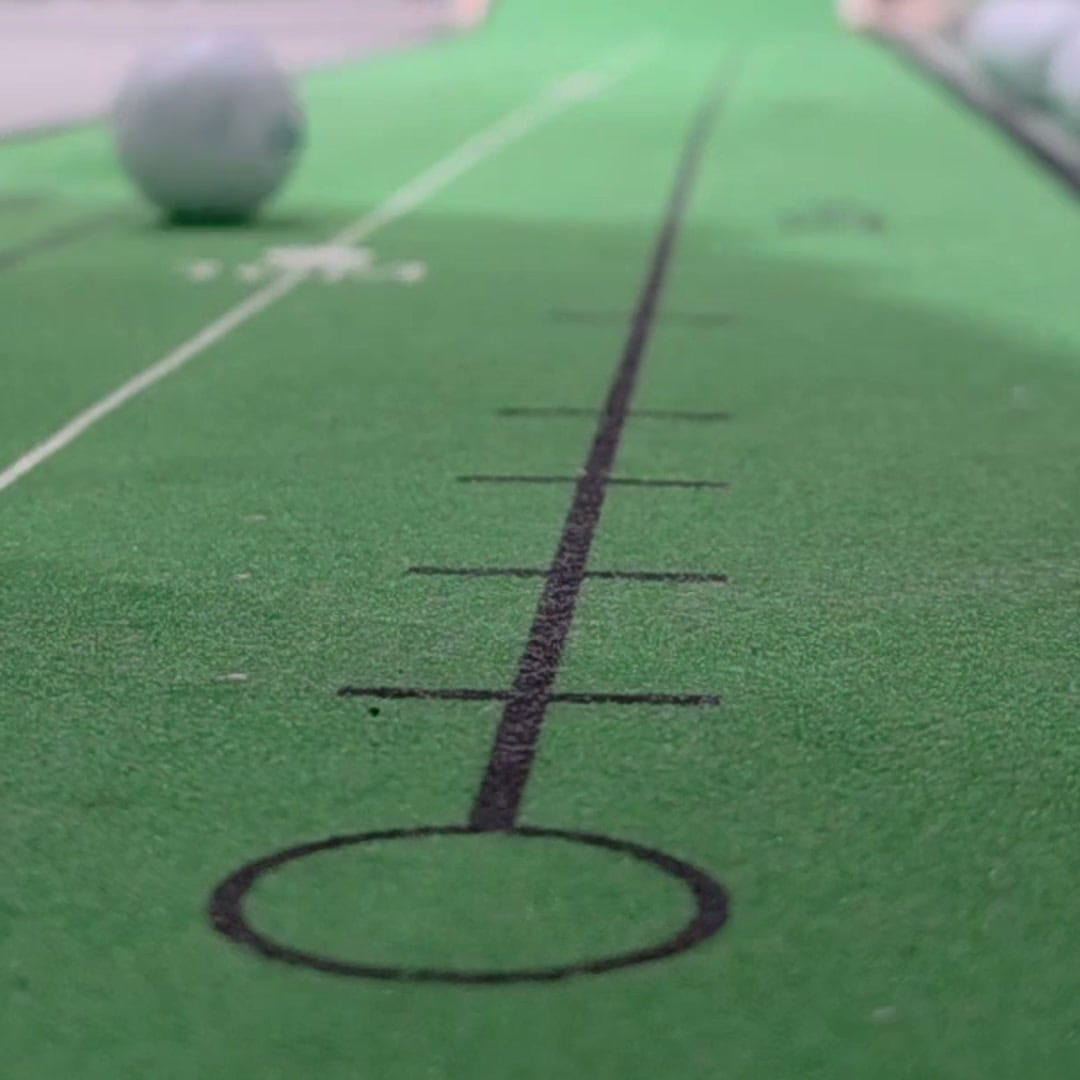 The printed target line of an indoor putting mat, with tick marks along its length and a target circle at the near end, running away from the camera.