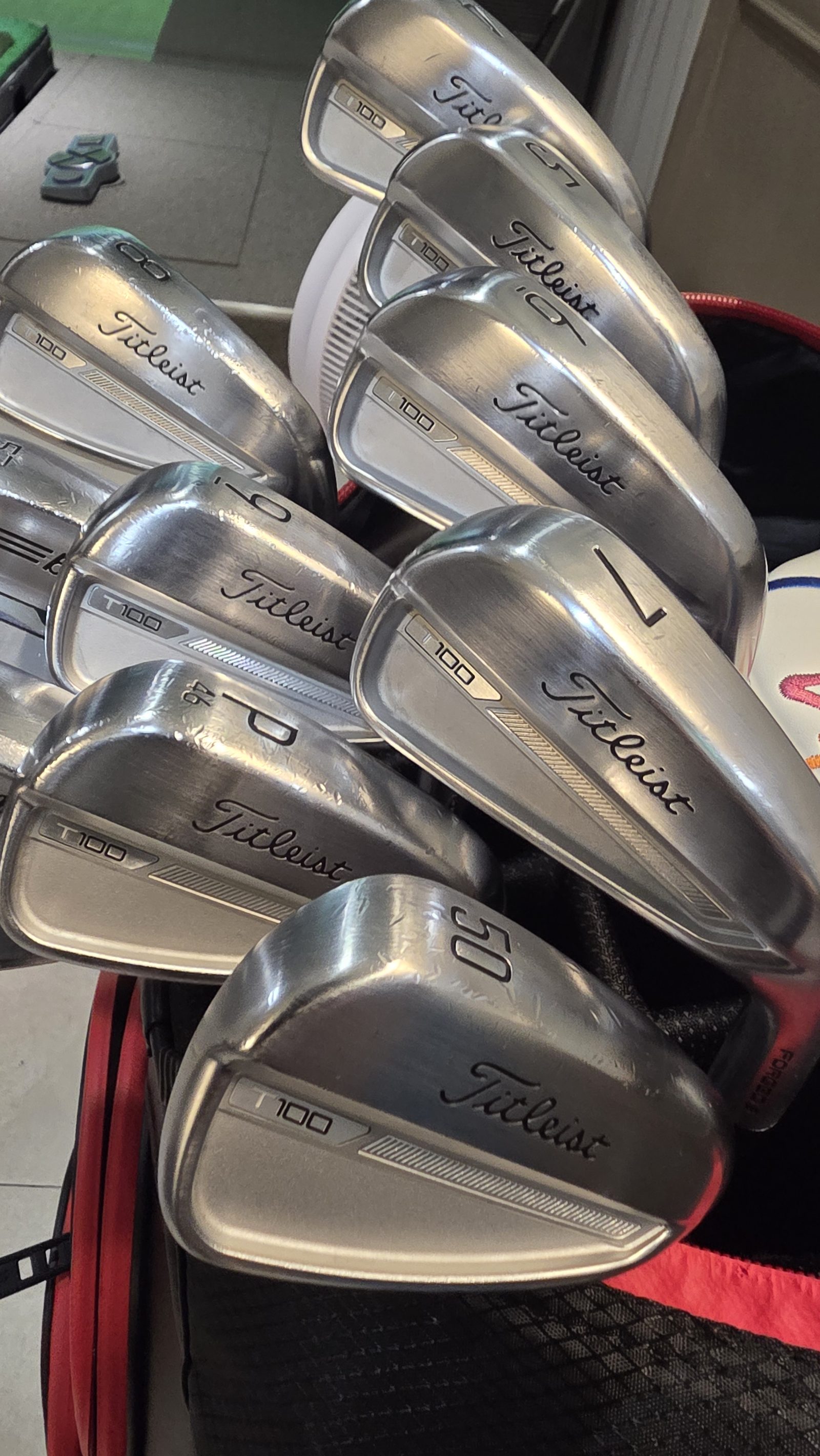 The author's Titleist T100 irons laid across a golf bag, with the pitching wedge stamped 46 and the gap wedge stamped 50 clearly visible.