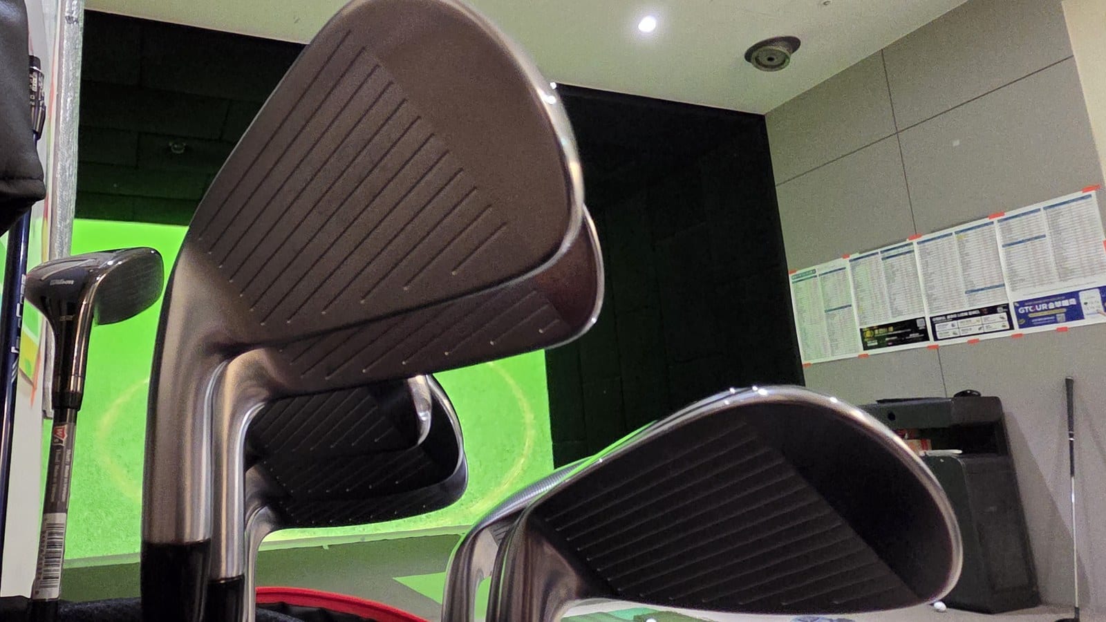 Two iron faces set up at an indoor screen golf bay, seen from ground level.