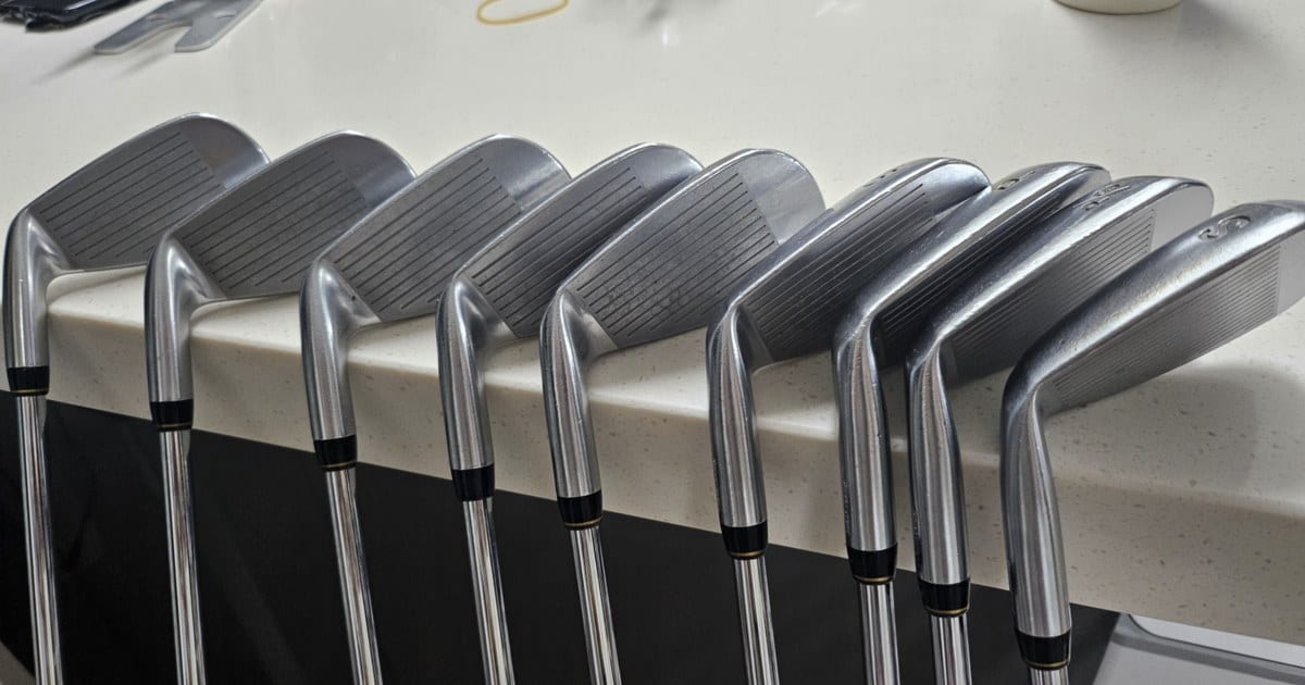 Nine Tourstage V300 III irons lined up on a kitchen counter, faces and toplines toward the camera.
