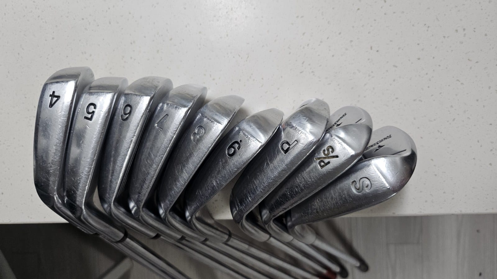 Nine Tourstage V300 III irons from behind, sole numbers 4 through S visible with the Tourstage name stamped on the back.