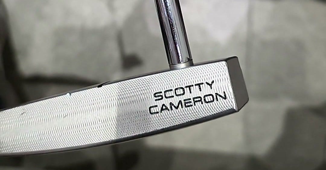 Extreme close-up of a Scotty Cameron Phantom X 5 face, the milled cross-hatch and the SCOTTY CAMERON stamp filling the frame, the shaft entering from above.