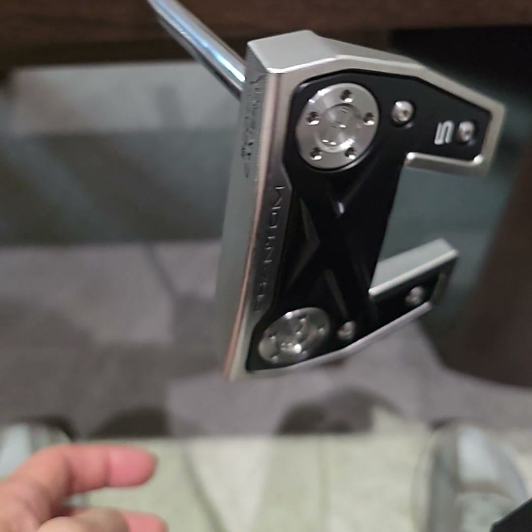 The sole cavity of a Scotty Cameron Phantom X 5, with PHANTOM X stamped along the flange, a model badge by the heel, two round sole weights and an X-shaped bridge between them.